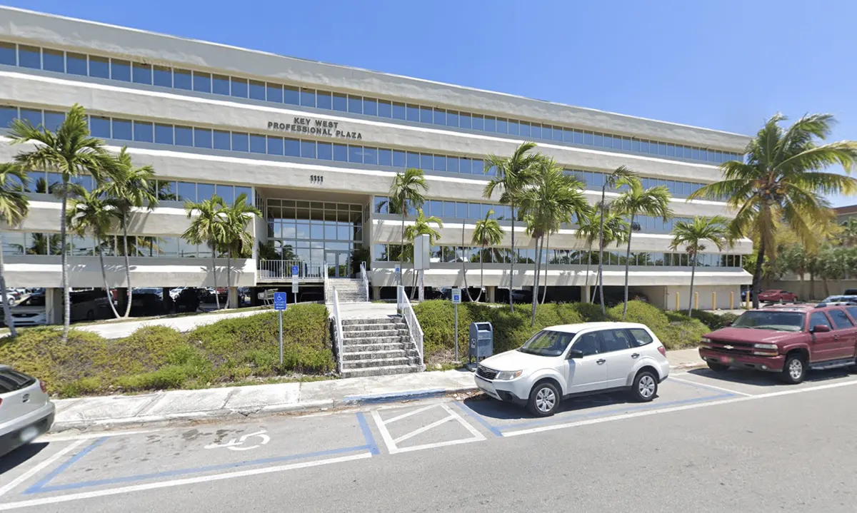 The Key West Professional Plaza, a multi-storey office building with palm trees and parked cars in front of it under a blue sky