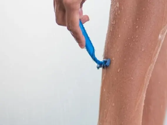 A leg being shaved with a blue razor under running water