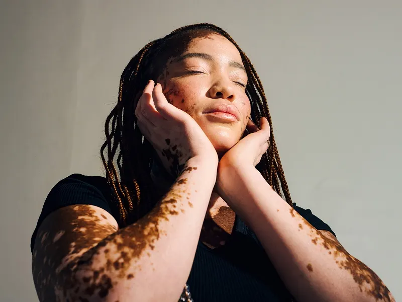 A woman with long dark hair and closed eyes, resting her face in her hands