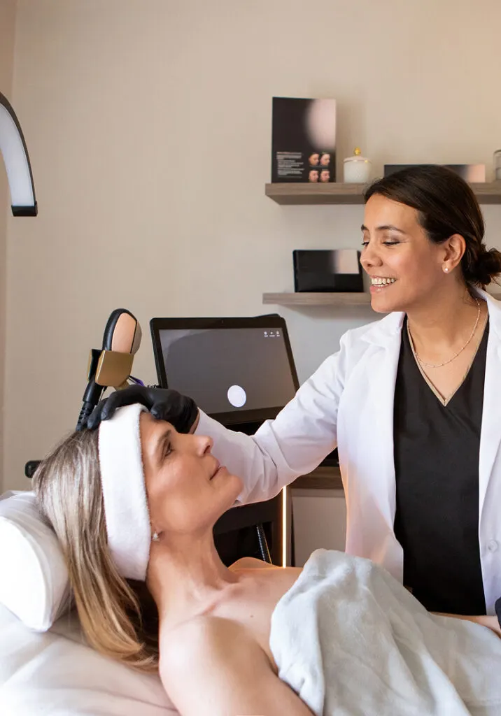 A woman lying back on a treatment bed while a clinician in a white coat works beside her in a bright room