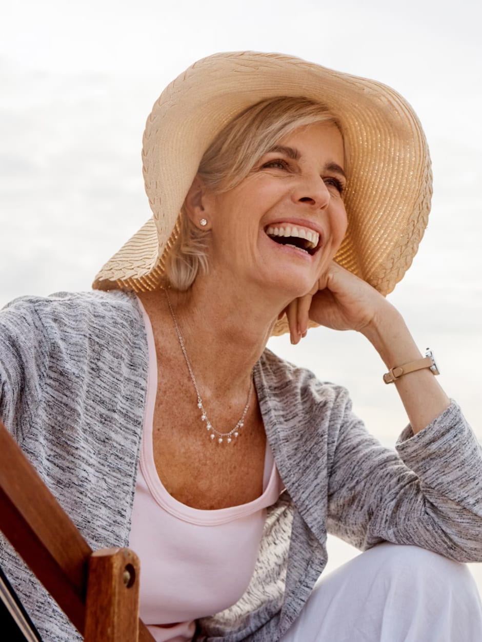 A smiling woman in a sun hat sitting by the sea