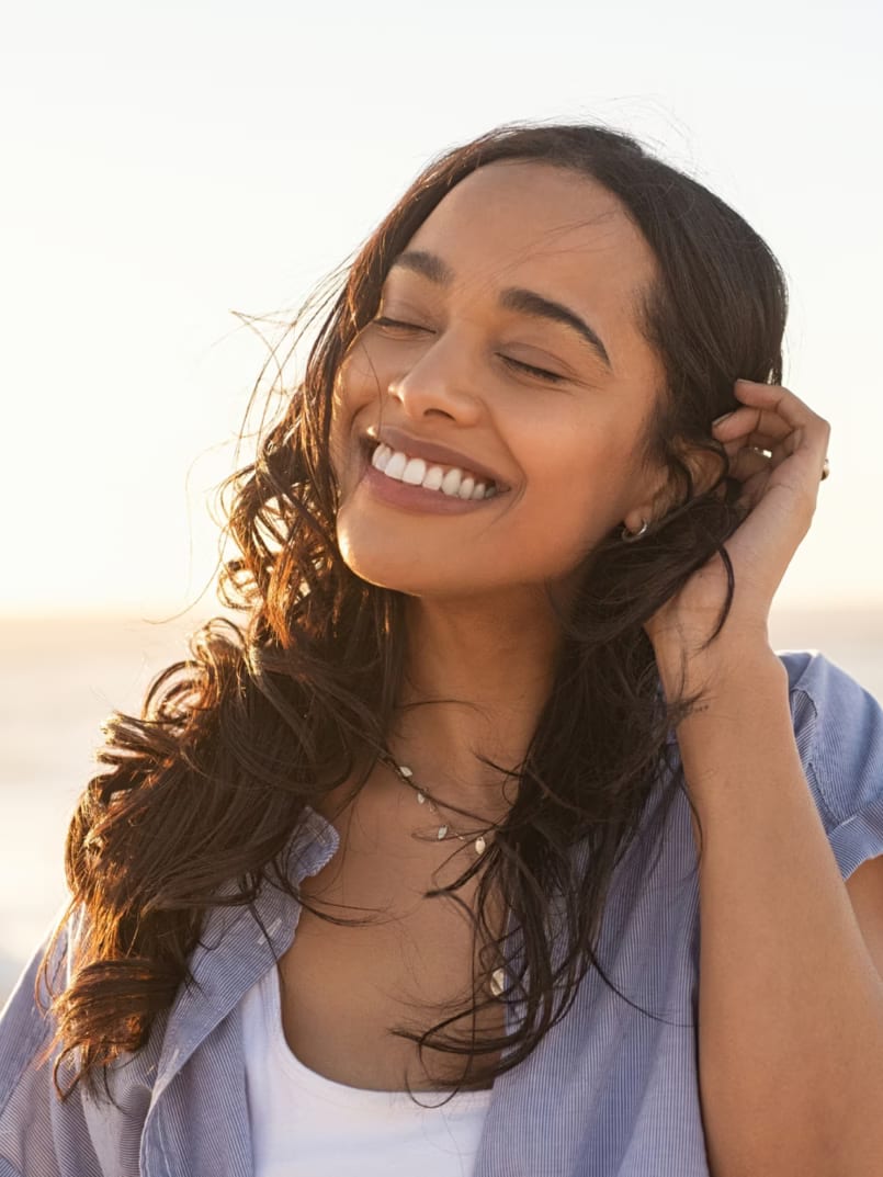 A smiling woman with long dark hair on a beach at sunset