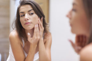 A woman looking at her face in a mirror and touching her cheek
