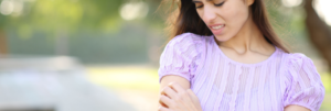 A young woman in a lilac blouse looking down at her forearm outdoors