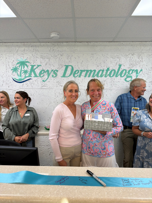 Two women holding a gift box in front of the Keys Dermatology sign at the front desk