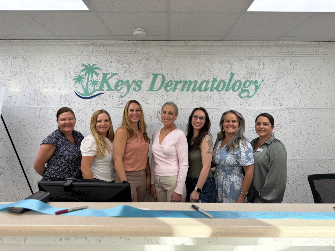 The Keys Dermatology team standing together at the Islamorada front desk, under the Keys Dermatology sign