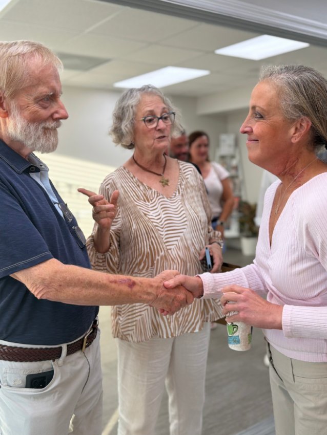 Two older women and an older man talking and shaking hands inside the new office