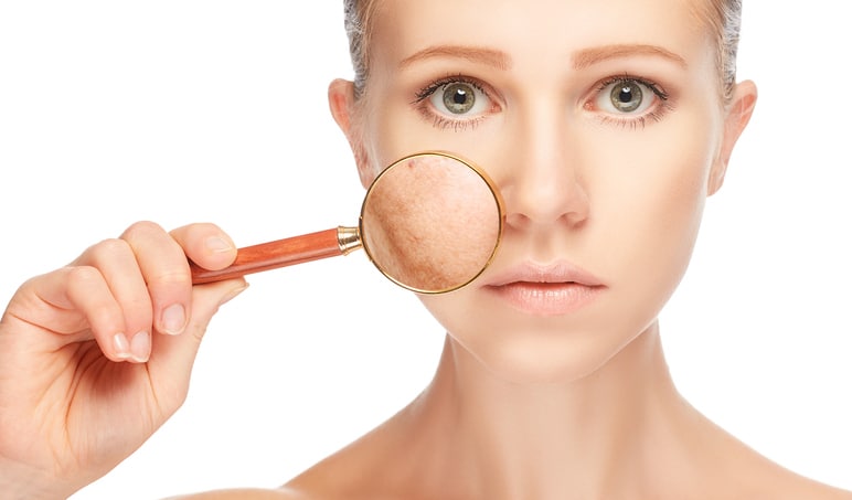 woman checking her skin with magnifying glass