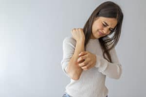 Women scratch the itch with hand , Concept with Healthcare And Medicine. Woman scratching arm on grey background. Allergy symptoms. Woman scratching her arm.