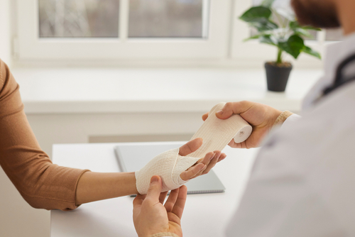 Doctor wrapping young woman's injured hand, close up